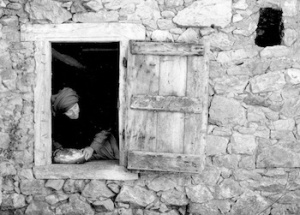 A woman appears in an open window in a stone house.